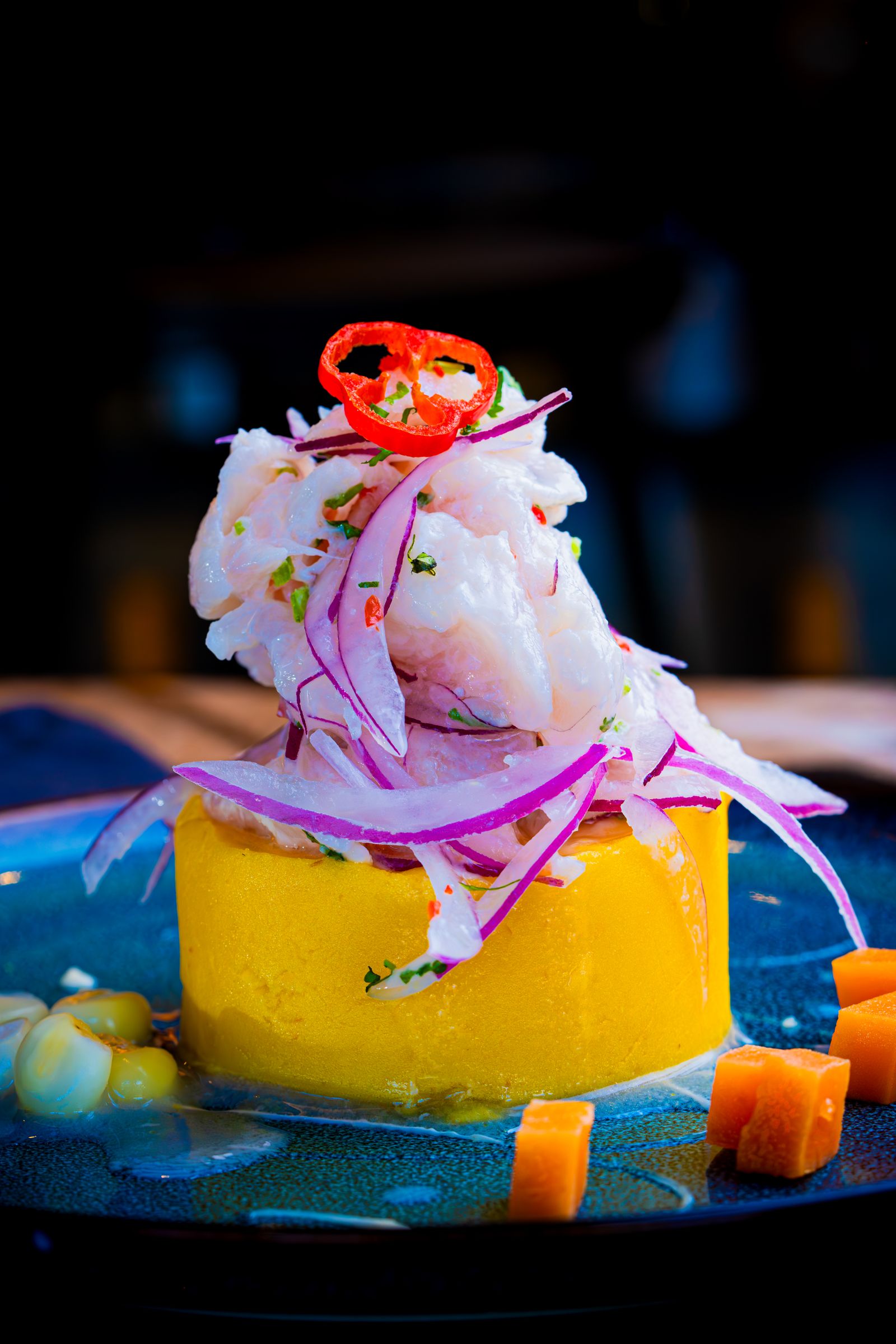 Ceviche on a blue plate with onion, chili, corn, and sweet potato